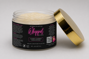 An open jar of Setoria Collective Whipped by Setoria Candy Chorus Sugar Scrub, featuring a black label with pink and white text and a metallic gold lid, set against a neutral gray background. 